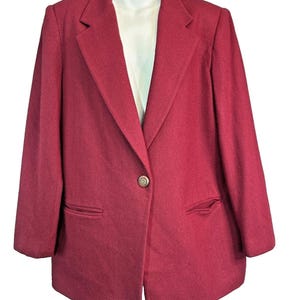 May include: A solid deep burgundy blazer featuring a single-button closure, notched lapels, and two horizontal welt pockets at the waist. The garment is constructed with long sleeves and a structured shoulder design, presented on a white mannequin.