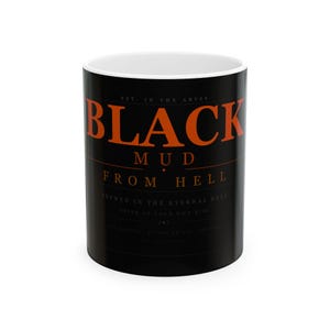 May include: A black ceramic mug with the words "BLACK MUD FROM HELL" in orange lettering. The mug also has the text "BREWED IN THE ETERNAL DARK" and "DRINK AT YOUR OWN RISK". The mug has a white interior.