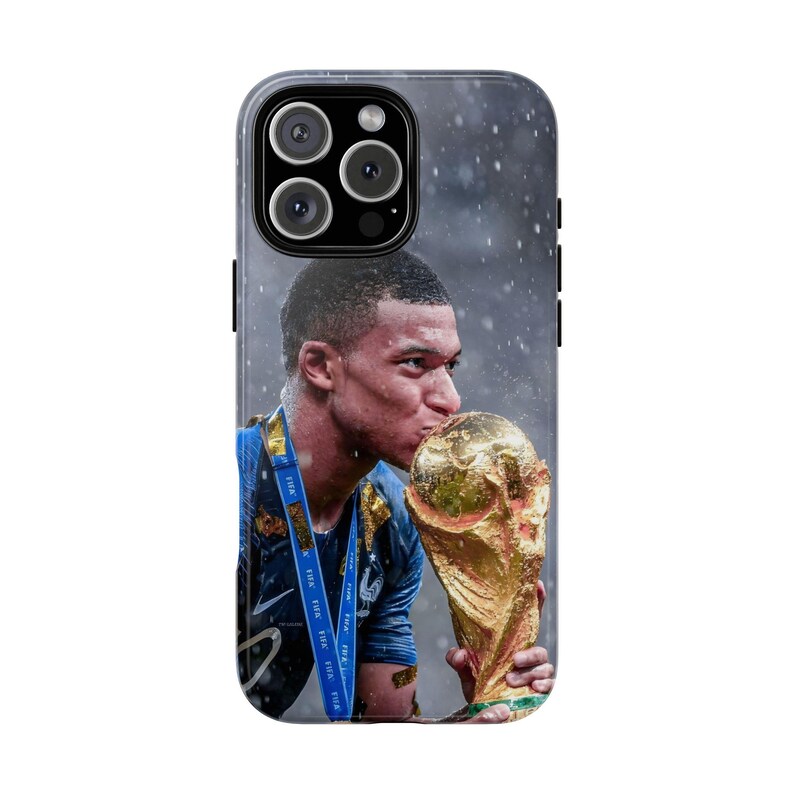 Pode incluir: Uma capa de smartphone com uma imagem de alta resolu&ccedil;&atilde;o de um jogador de futebol com uma camisola azul a beijar um trof&eacute;u dourado. O jogador usa um cord&atilde;o azul com o texto FIFA impresso. O fundo mostra uma atmosfera escura e chuvosa.