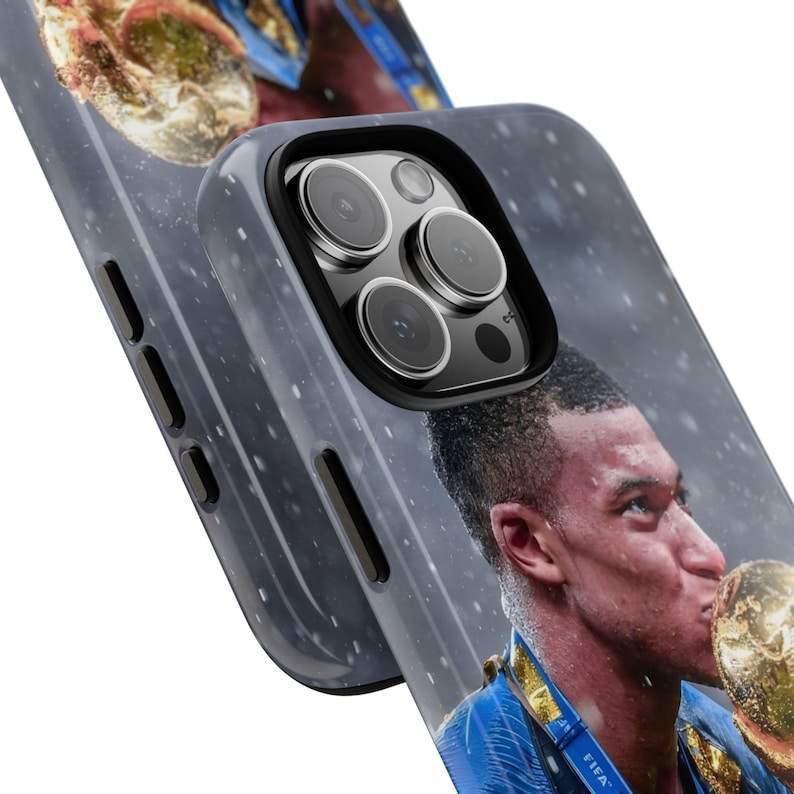 Pode incluir: Uma capa de smartphone cinza-escura com uma impress&atilde;o fotogr&aacute;fica de um jogador de futebol beijando um trof&eacute;u dourado. A capa possui um recorte para um sistema de c&acirc;mera tripla e bot&otilde;es laterais, com um sutil padr&atilde;o de manchas brancas.
