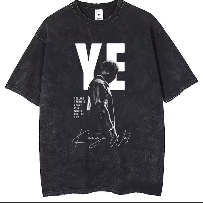 Op de afbeelding: Een zwart acid-wash t-shirt met een grote witte "YE"-afbeelding, een zwart-wit silhouet van een persoon, de tekst "TELLING TRUTH IS CRAZY IN A WORLD FULL OF LIES" en een witte handgeschreven handtekening "Kanye West".