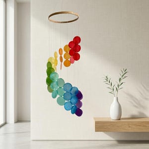 May include: A hanging mobile featuring a circular wooden frame with multiple translucent, colourful circular discs suspended by thin strings. The discs are arranged in a cascading rainbow gradient, transitioning from red and orange to yellow, green, blue, and purple.
