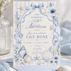 May include: A rectangular invitation card featuring a light blue and white striped background with a central arch frame tied with a blue ribbon. The design includes watercolor illustrations of seashells, starfish, and blue flowers with text reading THE SUMMER I TURNED Thirteen, Join us to celebrate LILY ROSE, SATURDAY JUNE 28TH 4:00PM, Seashell Cove, 245 Ocean Breeze Lane Charleston, SC 29401.