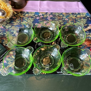 May include: A set of six translucent lime green glass bowls, each featuring a scalloped handle design on opposite sides. The bowls are arranged in two rows of three, displaying a smooth interior surface and a ribbed exterior pattern.