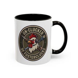 May include: A white ceramic mug with a black handle and rim, featuring a circular graphic of a rooster wearing a headset. Behind the rooster are crossed tools, and the text reads UN-CLUCKER OF FUSTERCLUCKS in a circular border around the design.