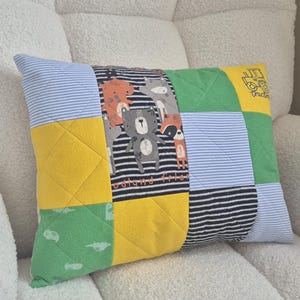 May include: A rectangular patchwork cushion featuring a variety of fabric squares in yellow, green, blue and white stripes, and a central panel with woodland animal illustrations and the text Woodland Friends, plus a small tractor graphic.