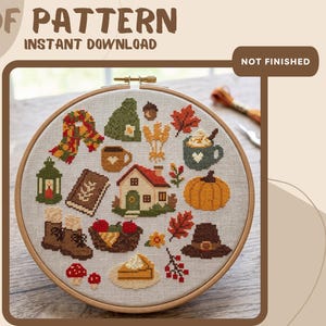 May include: A cross stitch pattern in a wooden embroidery hoop featuring autumn-themed icons including a house, pumpkin, scarf, boots, mushrooms, a book, and a lantern. The text reads PDF PATTERN INSTANT DOWNLOAD and NOT FINISHED.
