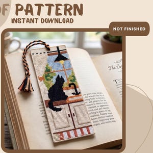 May include: A rectangular cross-stitch bookmark featuring a black cat sitting on a kitchen counter by a window. The design includes a hanging lamp, a faucet, and a striped floor pattern. A braided cord with a small tassel is attached to the top.