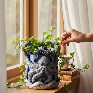 May include: A cylindrical blue ceramic planter featuring a three-dimensional octopus relief design with textured tentacles wrapping around the exterior. The base of the planter is sculpted to resemble stylized ocean waves in shades of white and grey.