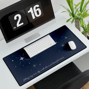 Könnte beinhalten: Eine rechteckige Schreibtischunterlage mit dunkelblauem Farbverlauf, weißen Sternillustrationen und dem Text "filling my own sky with the most beatiful stars" in weißer Schreibschrift im unteren rechten Bereich.