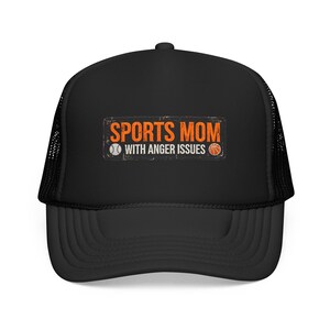 May include: A black trucker hat featuring a rectangular graphic with distressed orange text that reads SPORTS MOM and white text that reads WITH ANGER ISSUES, flanked by a white baseball icon and an orange basketball icon on a black mesh background.
