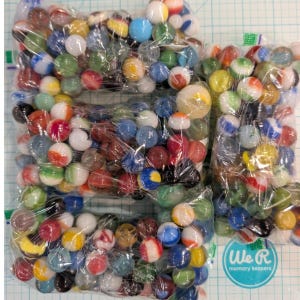 May include: A collection of glass marbles in various colors and patterns, including solid, swirled, and translucent designs, packaged in three clear plastic bags. The marbles are assorted in size and hue, featuring red, blue, green, yellow, and white.