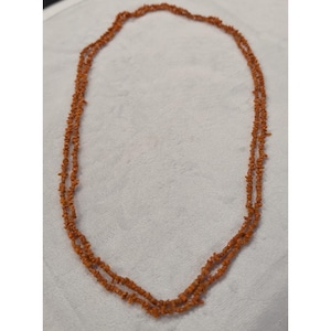 May include: A long, double-strand necklace composed of small, irregular, raw-cut orange stone chips. The necklace features a continuous loop design with no visible clasp, showcasing a uniform texture and a vibrant, earthy orange colour throughout.
