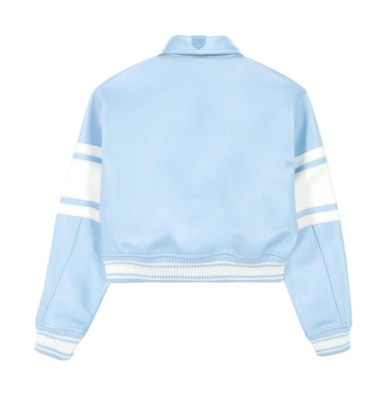 May include: A light blue varsity jacket featuring a classic collar, long sleeves with wide white horizontal stripes, and ribbed knit cuffs and hem with white and light blue stripes. The jacket has a smooth finish and a structured, cropped silhouette.