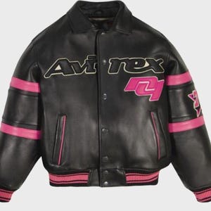 May include: A black leather varsity jacket featuring the text Avirex in white and black lettering across the chest. The jacket includes bright pink horizontal stripes on the sleeves, a pink graphic on the chest, and pink ribbed cuffs and hem.