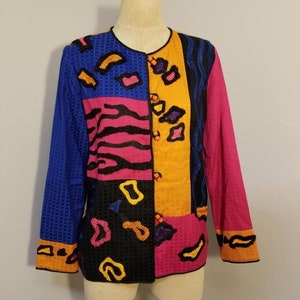May include: A colorful, multi-colored, patchwork jacket with a geometric design. The jacket is made of a textured fabric and has a button closure.