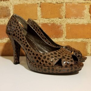 May include: A pair of brown peep-toe heels with a snakeskin pattern. The heels are high and have a platform.