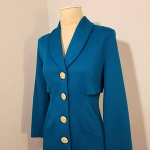 May include: A teal blue dress with a collared neckline and gold buttons. The dress has long sleeves and a fitted silhouette.