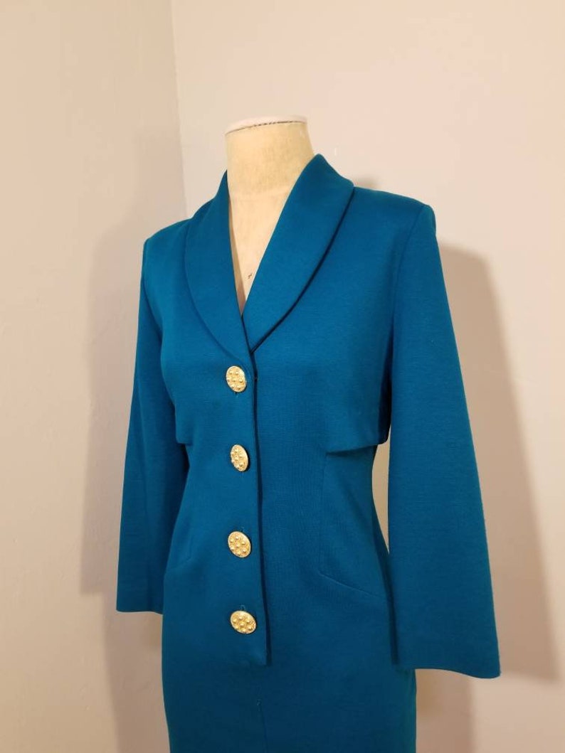 May include: A teal blue dress with a collared neckline and gold buttons. The dress has long sleeves and a fitted silhouette.
