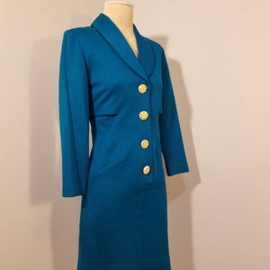 May include: Teal blue dress with a collar and gold buttons. The dress has a fitted silhouette and a knee-length hem.