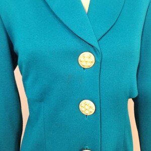 May include: Teal blazer with a notched collar and gold buttons. The buttons have a raised, circular design.
