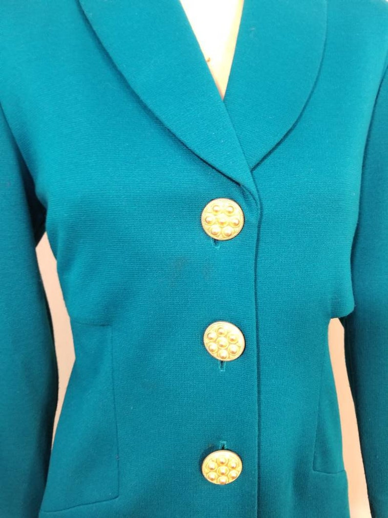 May include: Teal blazer with a notched collar and gold buttons. The buttons have a raised, circular design.