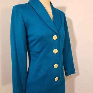 May include: A teal blue blazer with a collar and five gold buttons. The blazer is on a white mannequin.