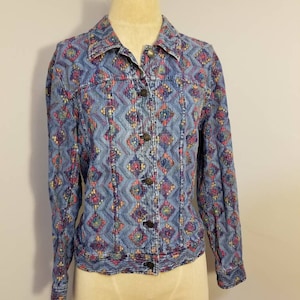 May include: A blue denim jacket with a colorful geometric pattern. The jacket has a button-up front and long sleeves.