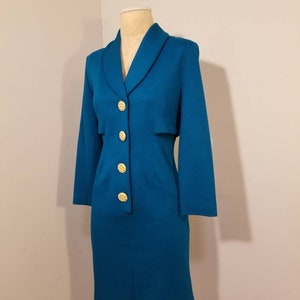 May include: A teal blue dress with a long sleeve and a collar. The dress has gold buttons down the front.