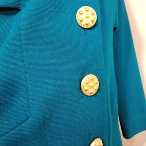 May include: Teal blue blazer with three gold tone buttons. The buttons have a raised, circular design.