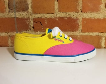 Könnte beinhalten: Gelbe und rosafarbene Canvas-Sneaker mit blauer Umrandung und weißer Sohle. Die Schuhe haben "Keds Spirit" auf der Seite.