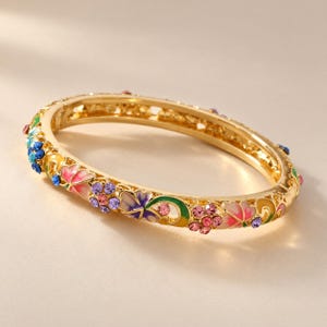 May include: A gold-tone hinged bangle bracelet featuring an intricate openwork design decorated with colorful enamel floral motifs in shades of pink, blue, purple, and green, accented with small embedded round crystals throughout.