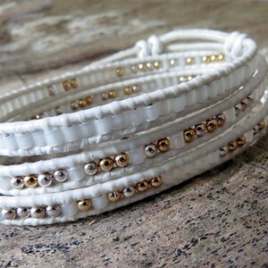 May include: White leather wrap bracelet with gold and silver beads.