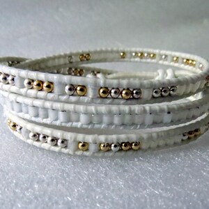 May include: White leather wrap bracelet with gold and silver beads.