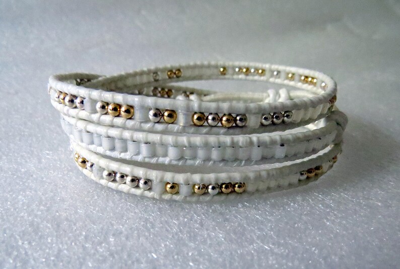 May include: White leather wrap bracelet with gold and silver beads.