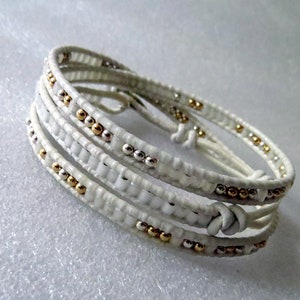 May include: White leather wrap bracelet with gold and silver beads.