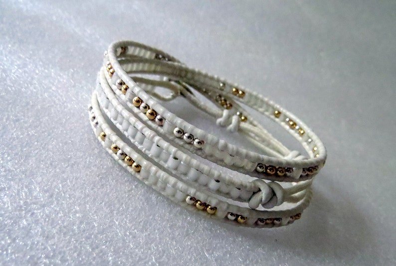 May include: White leather wrap bracelet with gold and silver beads.