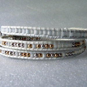 May include: White leather wrap bracelet with silver and gold beads.