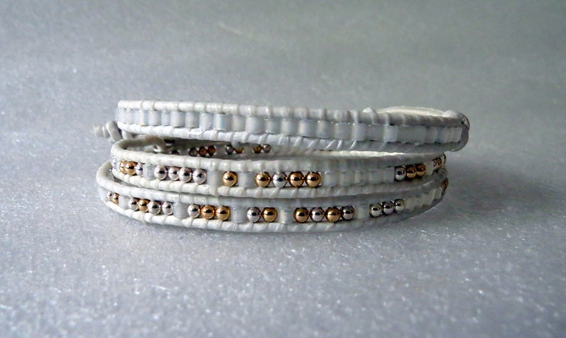 May include: White leather wrap bracelet with silver and gold beads.