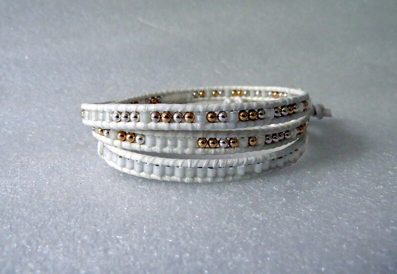 May include: White leather wrap bracelet with silver and gold beads.