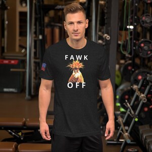 May include: Black t-shirt with the text "FAWK OFF" and a graphic of a rooster. The shirt has a small American flag on the left sleeve. The person is standing in a gym.