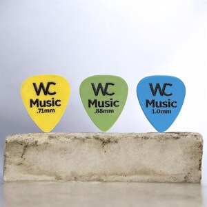 May include: Three guitar picks in yellow, light green, and blue, each featuring the black text WC Music and their respective thicknesses of .71mm, .88mm, and 1.0mm printed on the front. The picks are arranged in a row against a plain background.