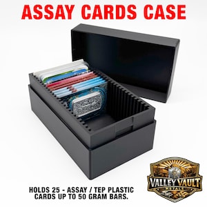May include: A black rectangular storage box with a removable lid, designed to hold assay cards. The interior features vertical slots for organizing cards and a small silver bar. Text on the image reads: ASSAY CARDS CASE, HOLDS 25 - ASSAY / TEP PLASTIC CARDS UP TO 50 GRAM BARS.