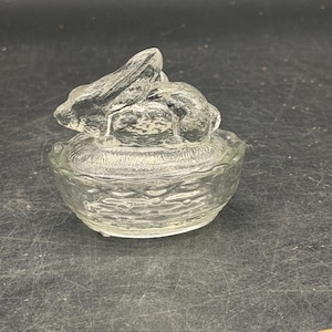 May include: A white ceramic mug with a black handle and the text "But First, Coffee" in a bold, black font. The mug is set against a blurred background, suggesting a cozy setting.