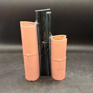 May include: A ceramic vase in a bamboo design. The vase features three vertical sections: two in a soft pink and one in glossy black. Each pink section has a decorative bow detail. The vase is a decorative item.