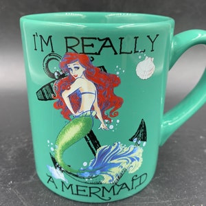 May include: A green ceramic mug with a handle. The mug features a graphic of Ariel, the Little Mermaid, with the text "I'm Really A Mermaid".