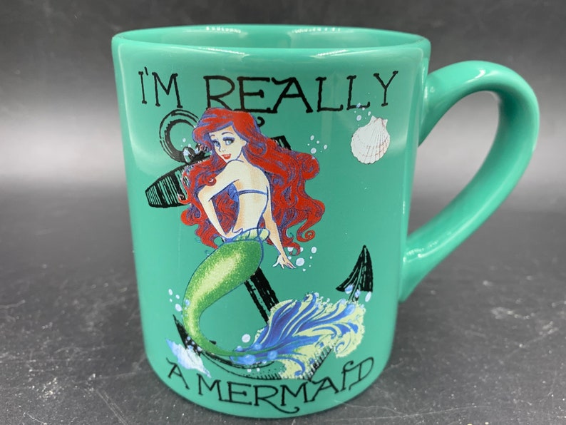 May include: A green ceramic mug with a handle. The mug features a graphic of Ariel, the Little Mermaid, with the text "I'm Really A Mermaid".