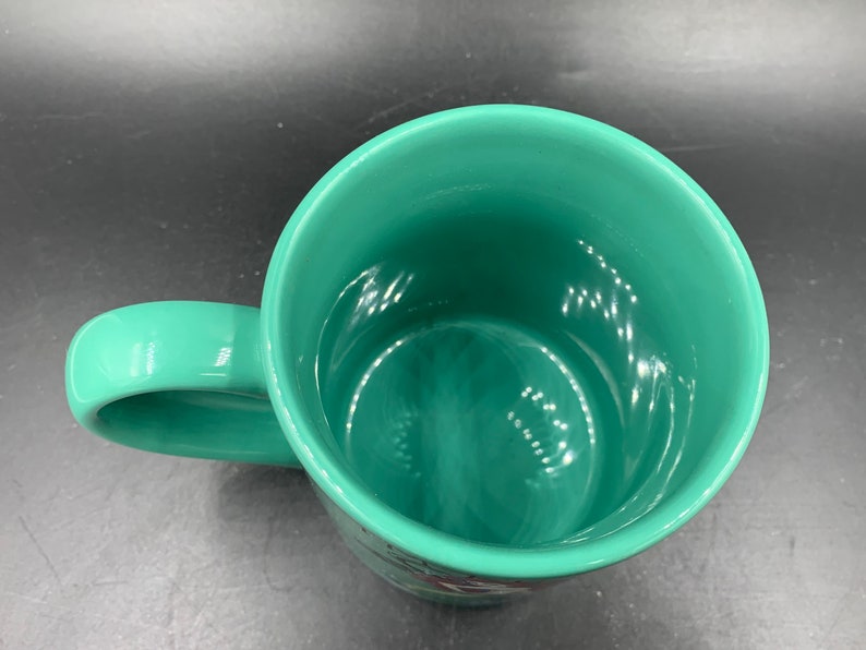 May include: A green ceramic mug with a smooth, glossy finish. The mug has a rounded handle and a wide, open mouth.