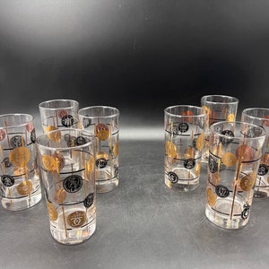 May include: Set of eight clear glass tumblers with a gold and black geometric pattern. The glasses have a mid-century modern design.