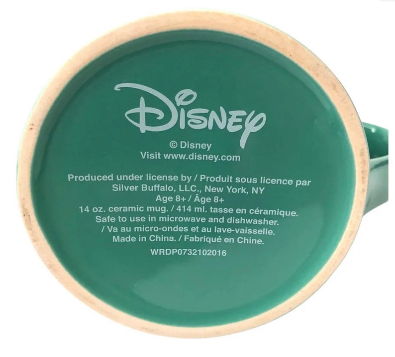 May include: Green ceramic mug with the Disney logo and text that reads "&copy; Disney Visit www.disney.com Produced under license by / Produit sous licence par Silver Buffalo, LLC., New York, NY Age 8+ / Age 8+ 14 oz. ceramic mug. / 414 ml. tasse en c&eacute;ramique. Safe to use in microwave and dishwasher. / Va au micro-ondes et au lave-vaisselle. Made in China. / Fabriqu&eacute; en Chine. WRDP0732102016"